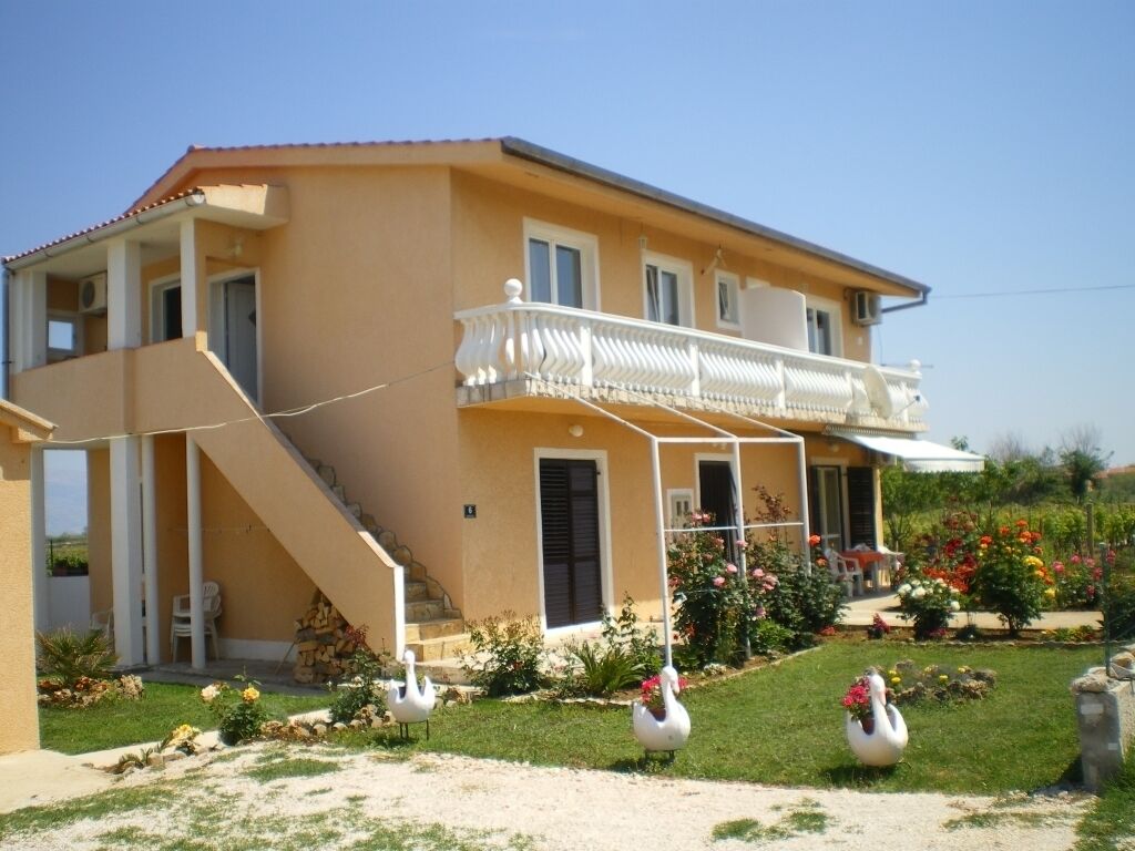A two-story house with a balcony, a staircase, and a garden with swans.