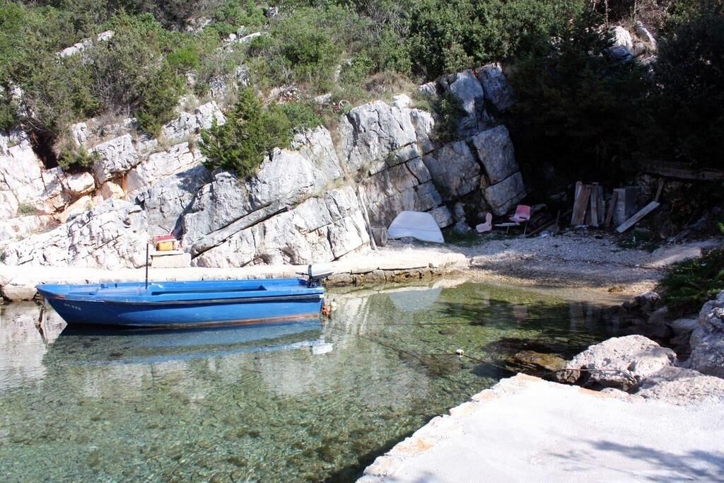 Una barca ormeggiata su una costa rocciosa con acque limpide, circondata da vegetazione naturale e rocce.