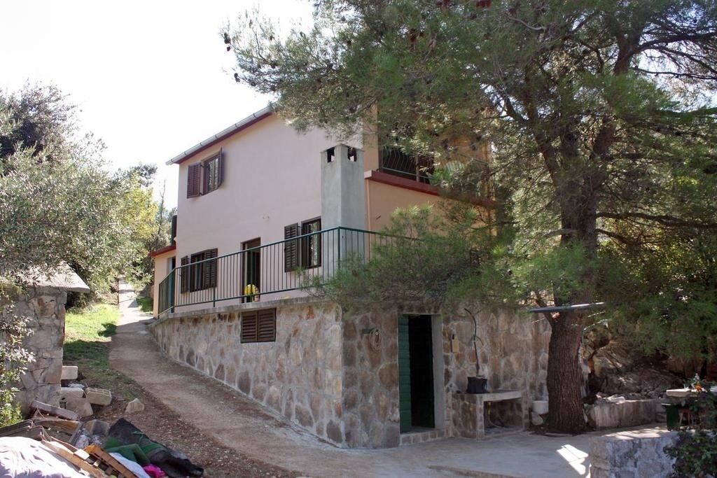 A stone building with a balcony, a door, and a small outdoor area with a table and chairs.