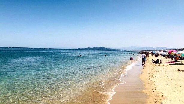 Una playa con agua cristalina, gente nadando y sombrillas en la arena.