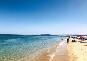 Ein Strand mit klarem Wasser, schwimmenden Personen und Sonnenschirmen im Sand.