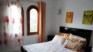 Un dormitorio con cama, cortinas, un ventanal y dos obras de arte en la pared.