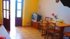 A compact living space with a bed, a dining table with chairs, a small television, and a kitchen area with a stove.