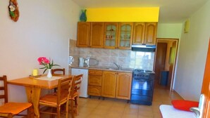 A compact kitchen with wooden cabinets, a dining table with chairs, a small refrigerator, and a stove.