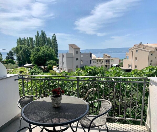 A balcony with a round table and two chairs, overlooking a residential area with buildings and greenery.