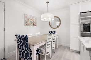 Un coin repas comprenant une table en bois, des chaises blanches, un luminaire suspendu, un miroir décoratif et un réfrigérateur.