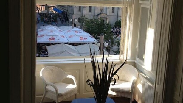 Ein Zimmer mit Blick auf eine Stadtlandschaft, ausgestattet mit einem Tisch, zwei Stühlen, einer Topfpflanze und einer Pendelleuchte.