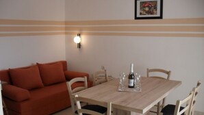 A dining area with a wooden table and four chairs, a red sofa, and a wall-mounted light fixture. - Apartment in Lopar with Terrace, Air condition, WIFI, Washing machine (87-2) (Lopar)