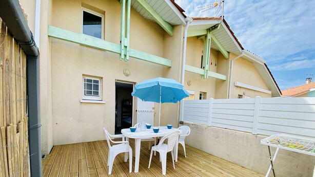 Un terrazzo in legno con tavolo e sedie, un ombrellone blu e un recinto bianco.