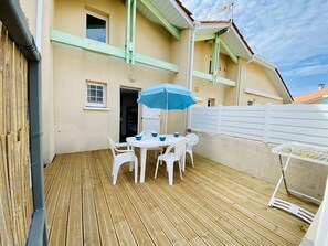 Una terraza de madera con una mesa y sillas, una sombrilla azul y una valla blanca.
