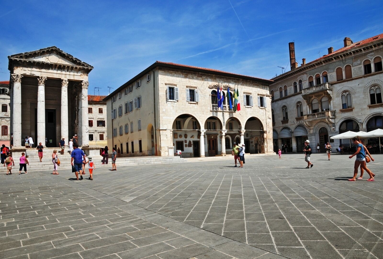 A spacious public square with historic buildings, including a prominent classical building with columns and a large arched entrance.