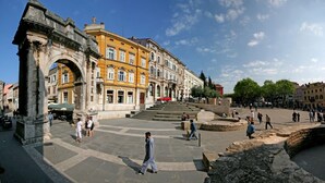 Ein öffentlicher Platz mit historischer Architektur, darunter ein Bogen und ein Brunnen.