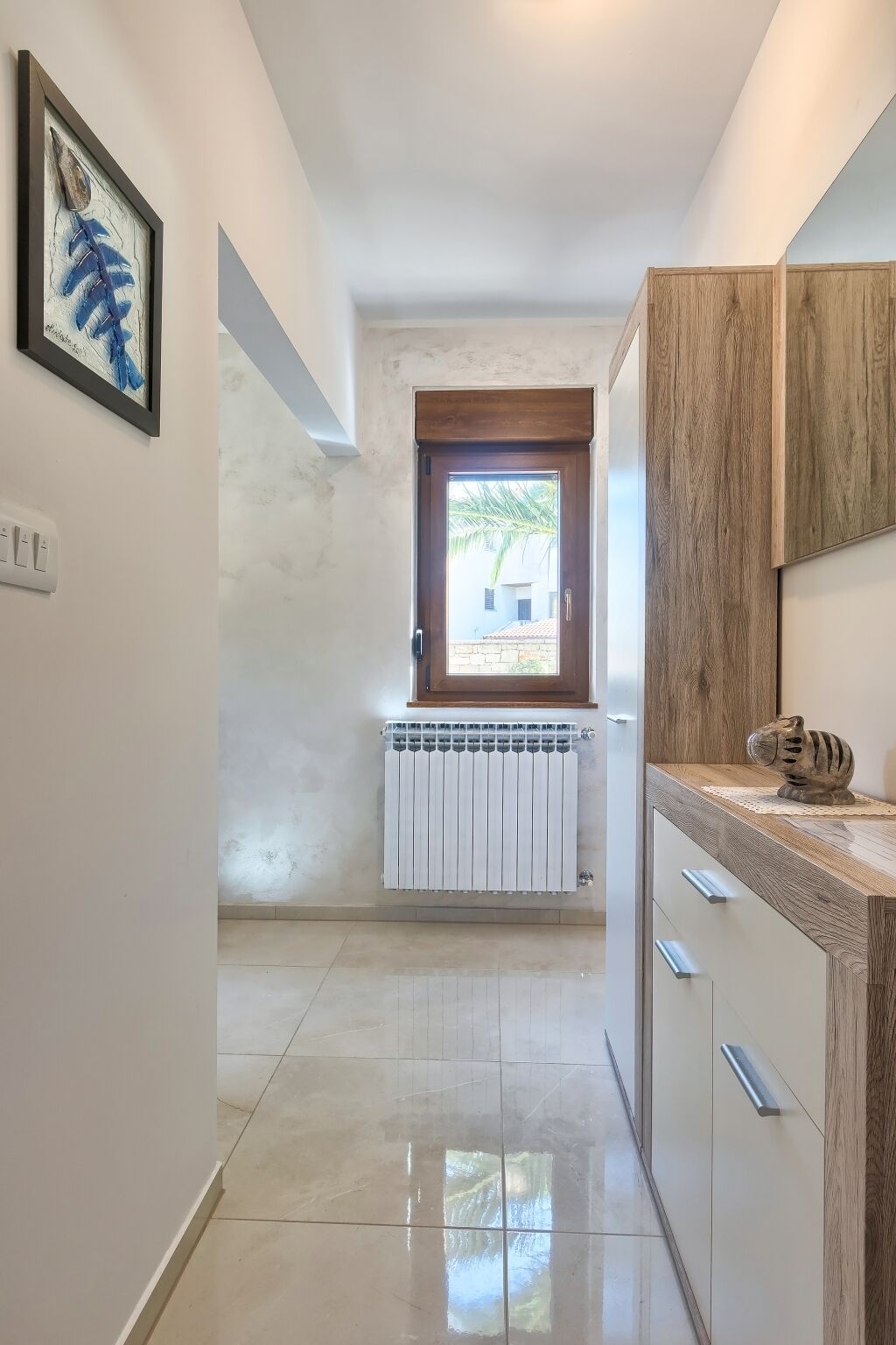 Un corridoio stretto con termosifone, un armadietto in legno e un quadro appeso al muro.