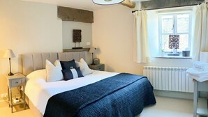 A bedroom with a large bed, bedside tables, a dresser, a window with curtains, and a radiator. - The Owlery at Aysgarth (Aysgarth, near Leyburn)