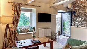 A cozy living room with a sofa, a coffee table, a lamp, a TV, and a window with curtains. - The Owlery at Aysgarth (Aysgarth, near Leyburn)