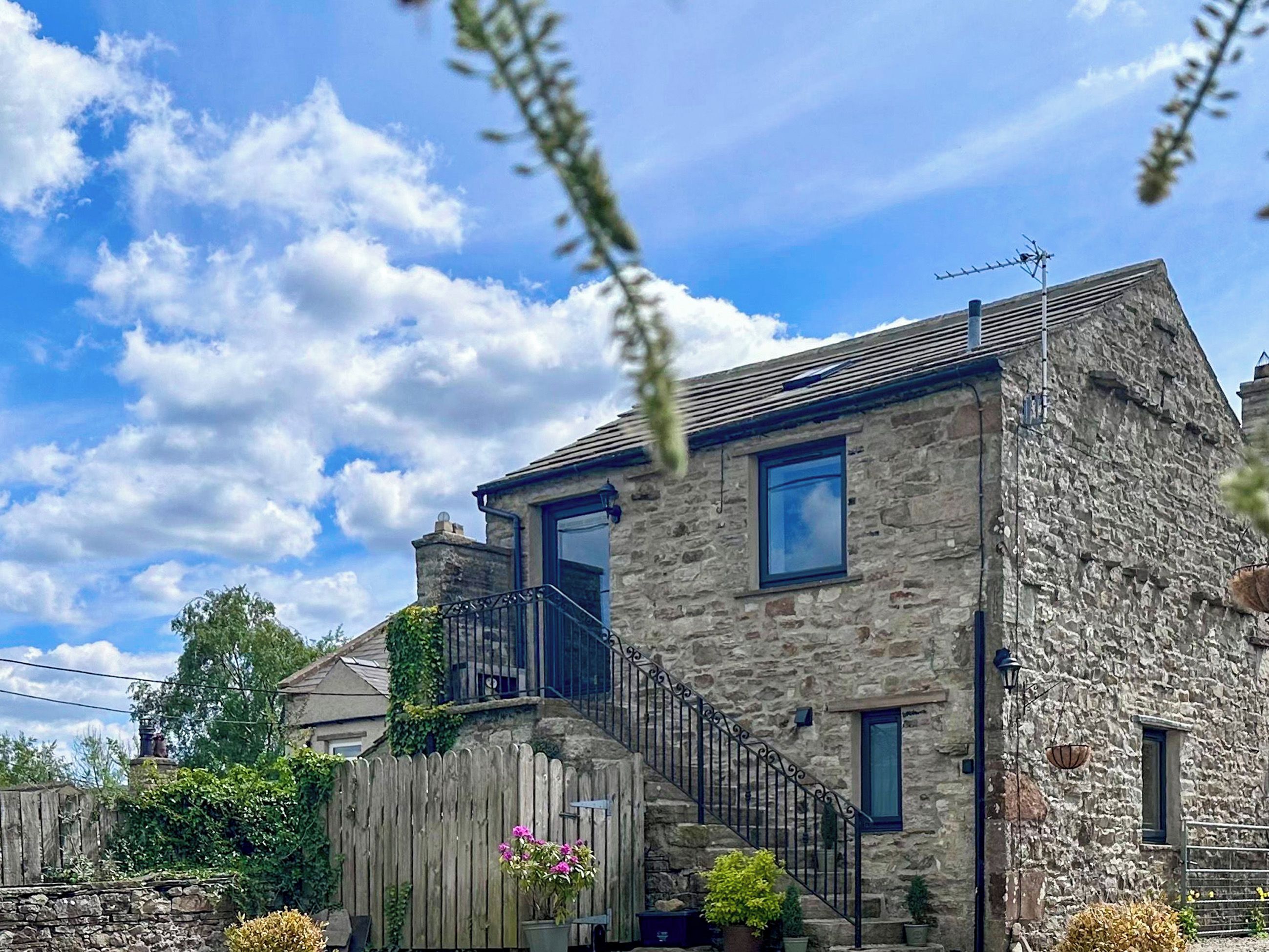 A stone house with a wooden fence, a balcony, and potted plants.