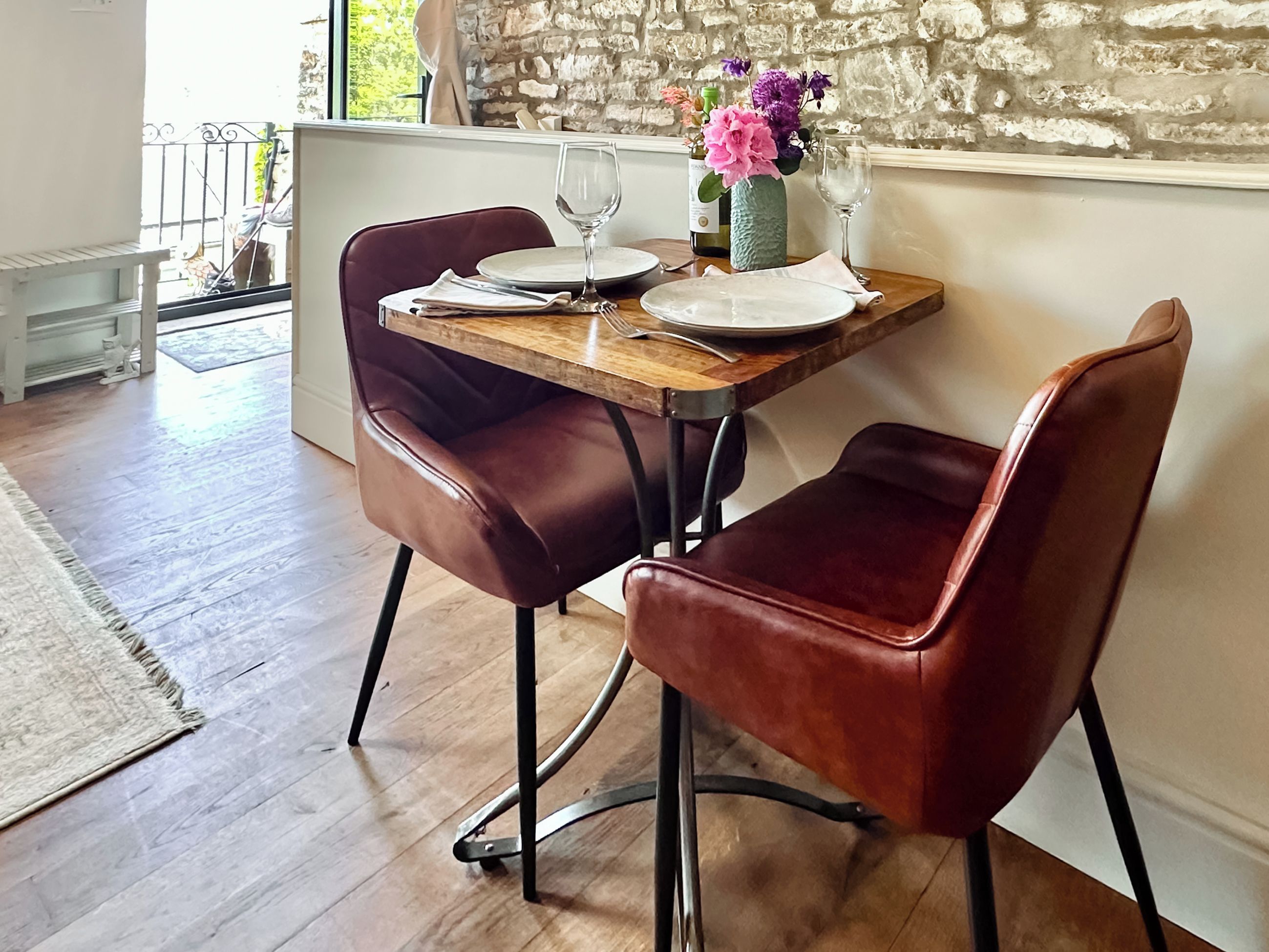 A dining table with two leather chairs, a vase with flowers, and a bottle of wine.