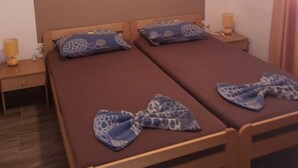 Un lit double avec un matelas marron et deux oreillers à motif girafe bleu. Il y a deux tables de chevet avec des lampes, un climatiseur fixé au mur et un plancher en bois.