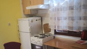 Une cuisine compacte équipée d’une cuisinière, d’un four et d’un réfrigérateur. On y trouve une table et une chaise en bois.