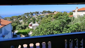 Vista costera desde un balcón con barandilla, que domina una colina con edificios y vegetación.