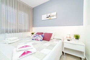 A neatly made bed with a checkered bedspread, a bedside table with a lamp and a plant, and a window with sheer curtains. - 0015-BAHIA Apartment in front of the beach with wifi (Empuriabrava)