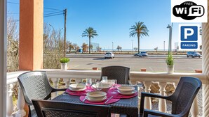 Un balcon avec une table dressée pour le dîner, donnant sur une rue bordée de palmiers et où sont garées des voitures.