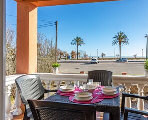 A balcony with a table set for dining, overlooking a street with palm trees and parked cars.