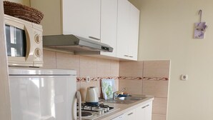Une cuisine compacte avec des meubles blancs, un four à micro-ondes, une bouilloire et une cuisinière.