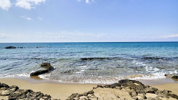 Una playa con agua azul cristalina, costa rocosa y una zona arenosa.