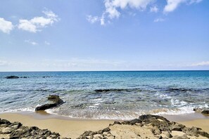 Ein Strand mit klarem Wasser, Felsen und einem sandigen Ufer.