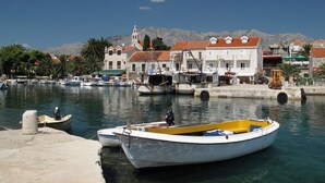 A marina with boats docked, a church with a bell tower, and buildings with red-tiled roofs.