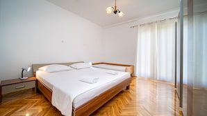 A modern bedroom with a wooden bed, a bedside table with a lamp, and a large window with curtains. - Apartment in Lopar with Terrace, Air condition, WIFI, Washing machine (129-1) (Lopar)