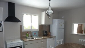 A compact kitchen with a stove, sink, and refrigerator. There is a dining table with chairs and a window above the sink. - Independent house, 3 bedrooms, 6 people, private pool in Lacanau ocean (LACANAU OCEAN)
