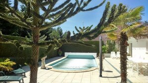 A pool area with a rectangular pool, surrounded by palm trees and a white building in the background. - Independent house, 3 bedrooms, 6 people, private pool in Lacanau ocean (LACANAU OCEAN)