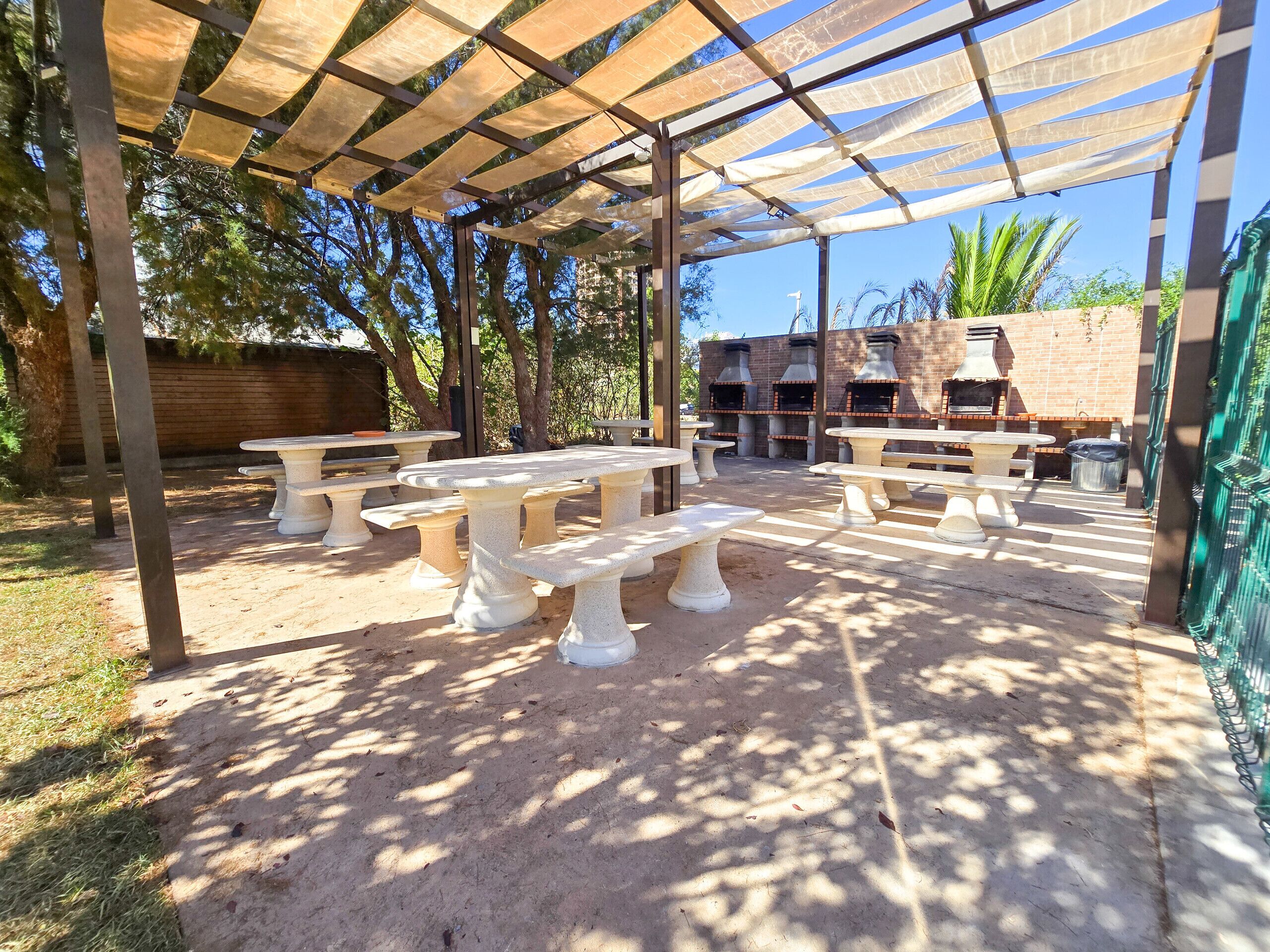 An outdoor patio area with stone tables and benches, a covered seating area, and a brick wall with a chimney.