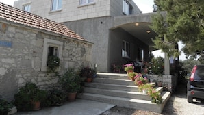 Un edificio a due piani con facciata in pietra e tetto in tegole. Scale conducono a un ingresso coperto, con vasi di piante e fiori.