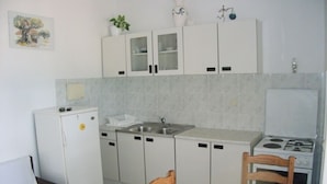 Una cucina compatta con mobili bianchi, un lavello, un fornello e un'area pranzo con due sedie di legno.