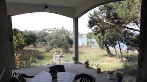 Un patio coperto con tavolo e sedie, piante in vaso e vista su un lago e alberi.
