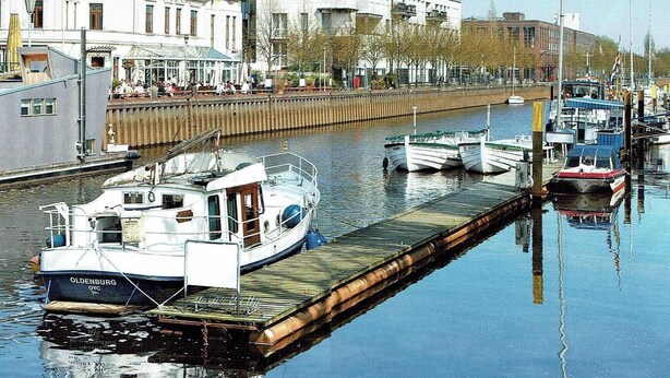 Un cours d’eau paisible où sont amarrés des bateaux, avec une jetée en bois et des bâtiments en arrière-plan.