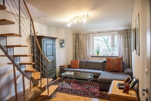 Una sala de estar con una escalera, un sofá, una mesa de centro y una ventana con cortinas.