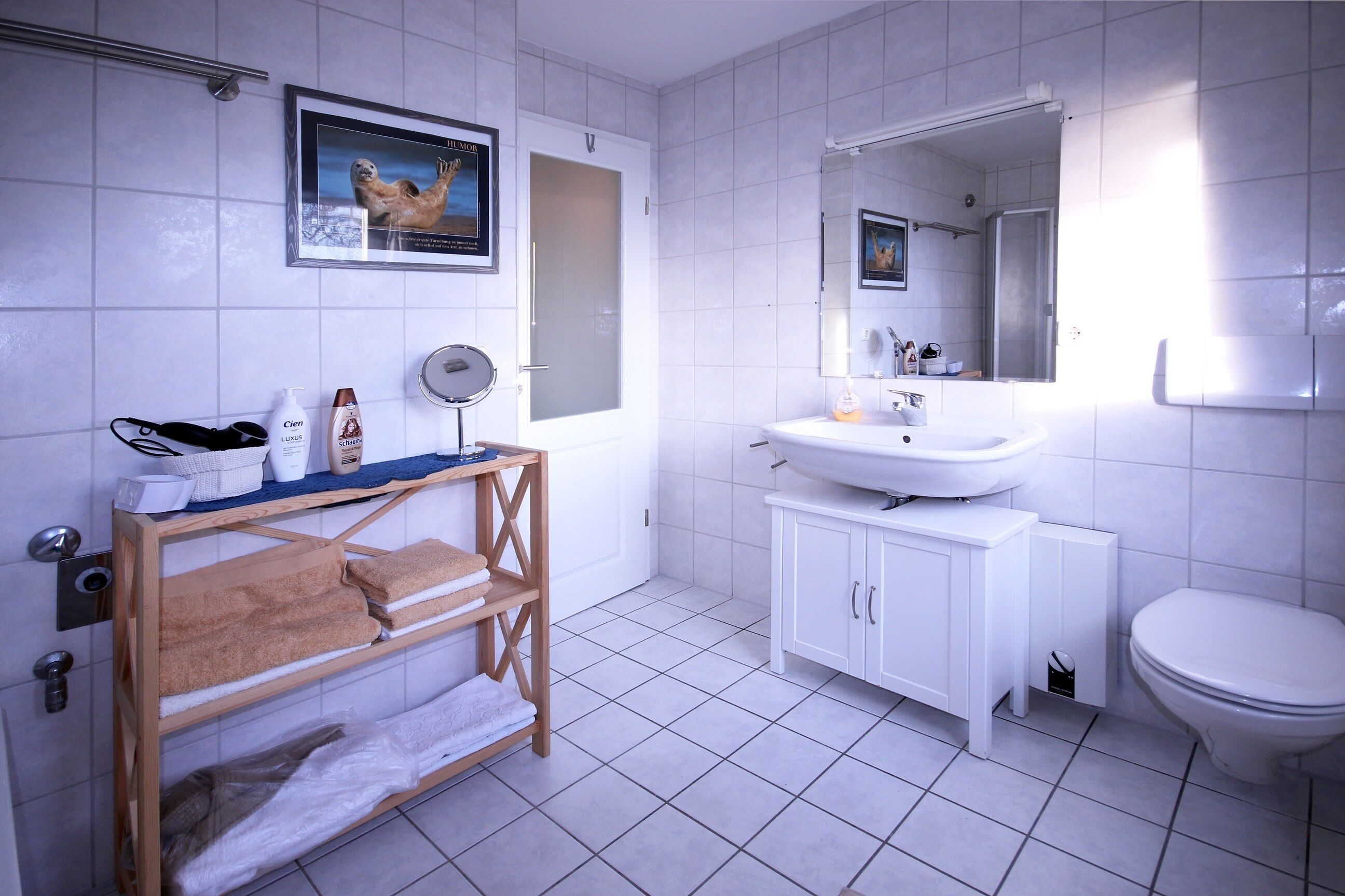 A modern bathroom with white tiles, a wooden vanity, a sink, a toilet, and a mirror.