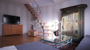 Un salon avec un escalier en bois, un téléviseur, une table basse en verre et une porte traditionnelle ornée de motifs floraux.