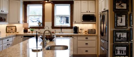 A kitchen with white cabinets, a large island with a sink, a microwave, a refrigerator, and framed pictures on the wall.