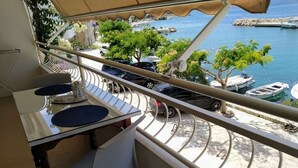 Un balcon avec une table et des chaises, donnant sur une marina où sont amarrés des bateaux et où abondent les espaces verts.