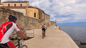 A paved walkway beside a body of water with stone walls and a building in the background.