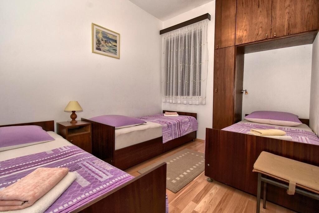 Een kleine, net kamer met twee eenpersoonsbedden, een houten garderobe, een bureau en een raam met dunne gordijnen.