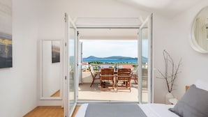 Ein Schlafzimmer mit Bett, Nachttisch, Spiegel und Blick auf einen Balkon mit Tisch und Stühlen.