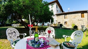 An outdoor dining area with a table set for two, surrounded by white chairs, a stone building in the background, and a tree providing shade. - Villa in Uzzano with 4 bedrooms sleeps 10 (Uzzano)
