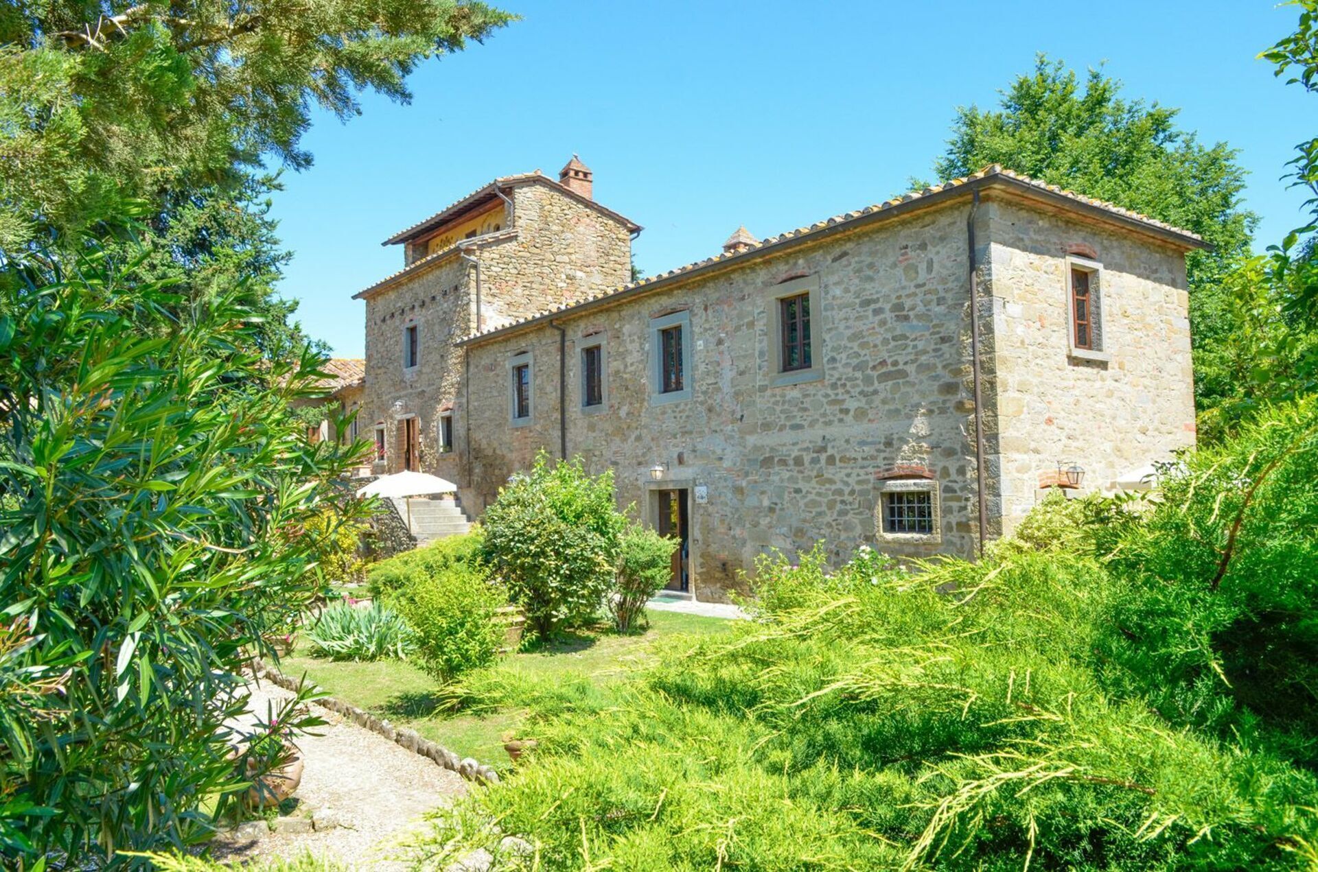 A stone building with a central tower, surrounded by lush greenery and a gravel path.