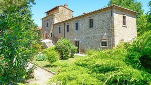 A stone building with a central tower, surrounded by lush greenery and a gravel path. - Relax and peace in Cortona with Pool (Cortona)